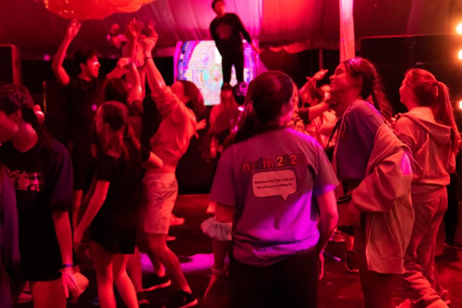 Students dance in a tent. The back of one person’s shirt says “nudm 2022” in lowercase letters.
