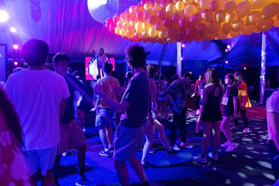 Students dance in a tent with orange and yellow balloons suspended in a bag from the ceiling.