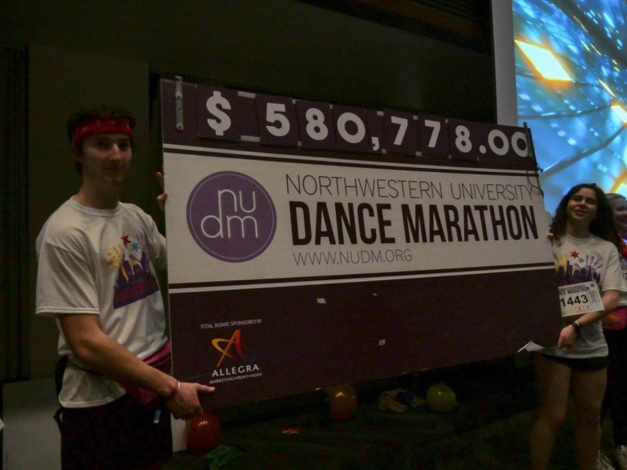 Two students hold a large cardboard check for $580,778.00. 