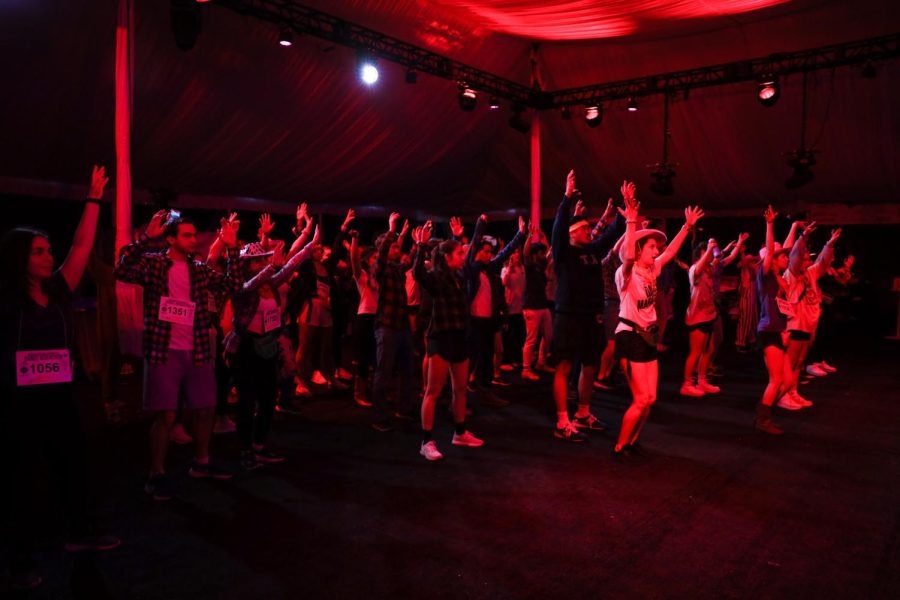 Underneath pink lighting in a tent, a group learns a dance. 
