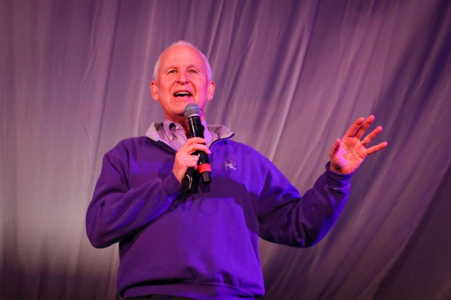 A man in a purple quarter zip speaks into a microphone.