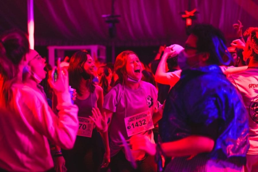 People dance under pink and blue lights in a tent.