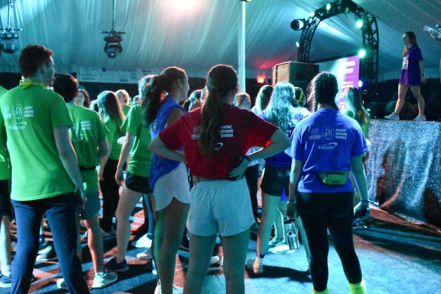  A crowd of people in red, green and blue shirts standing facing a stage. 