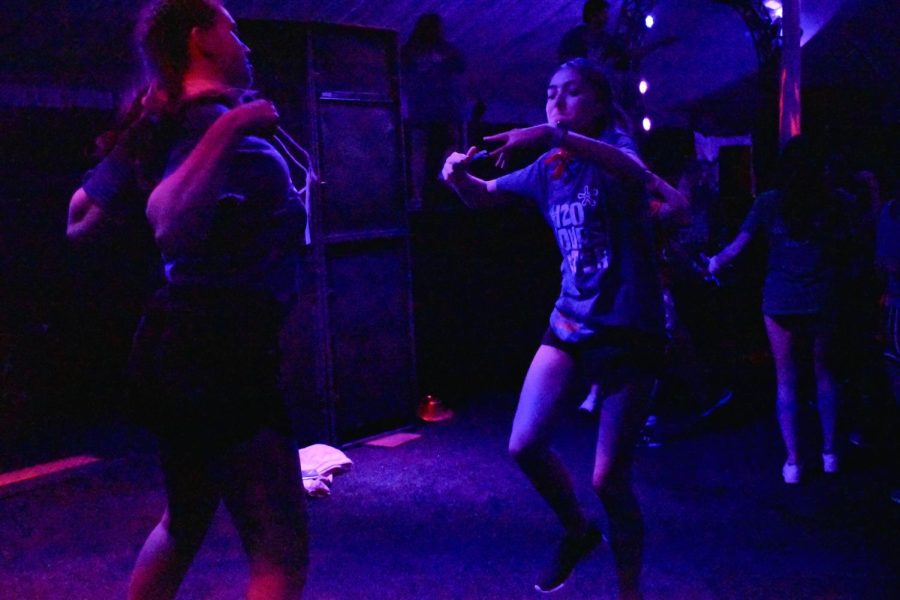 Two people in shorts and blue shirts dancing with their arms bent in front of them. 