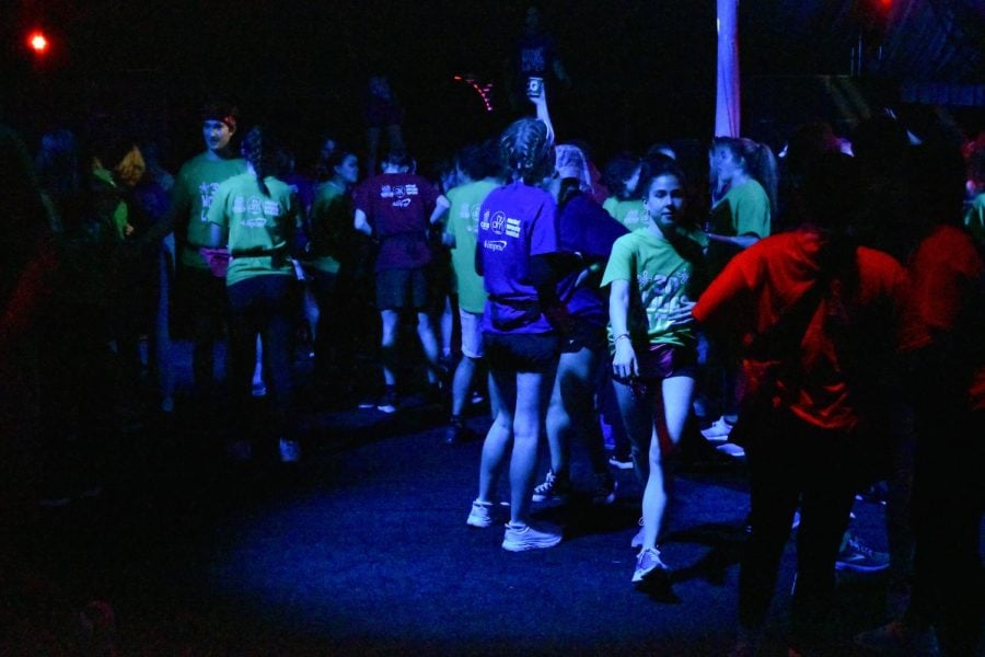 A crowd of people on the dance floor in red, green and blue shirts. 