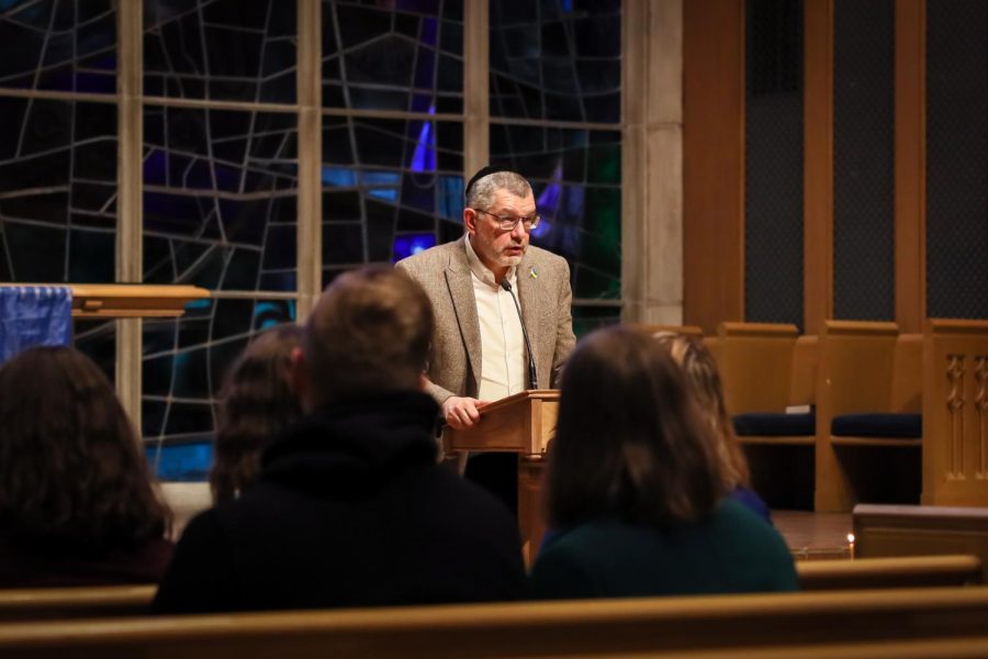 Someone in a gray jacket speaks at a chapel in front of a stained glass window.