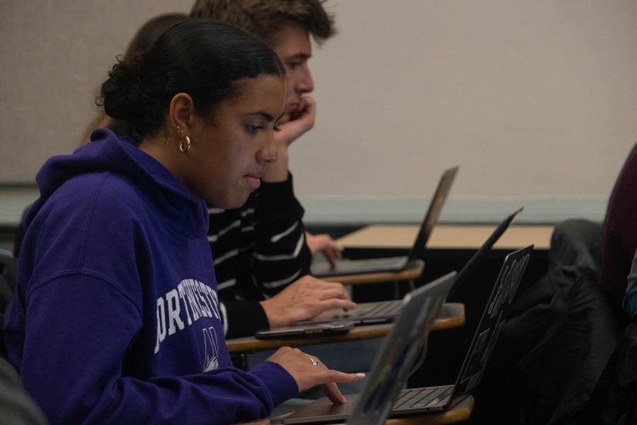 A student wearing a purple Northwestern sweatshirt sits in a classroom and works on her computer.