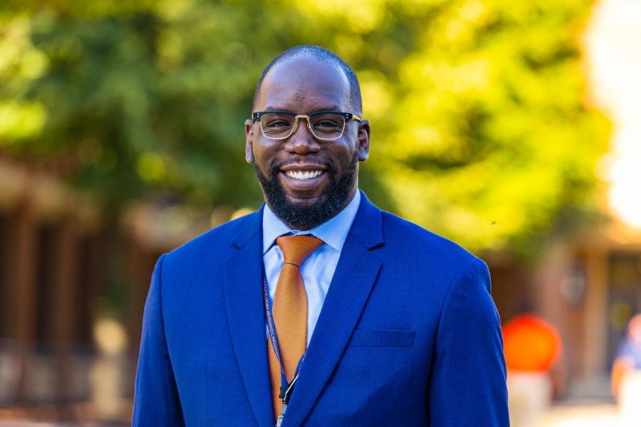 Marcus Campbell smiles facing the camera. He is wearing a blue blazer and an orange tie.