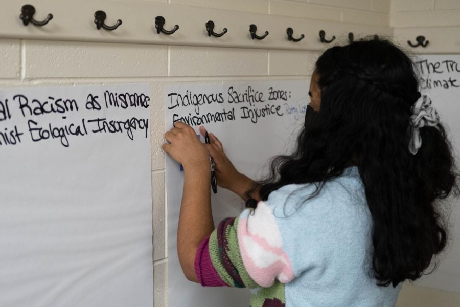 A participant writes on a poster that says “Indigenous Sacrifice Zones: Environmental Injustice.”