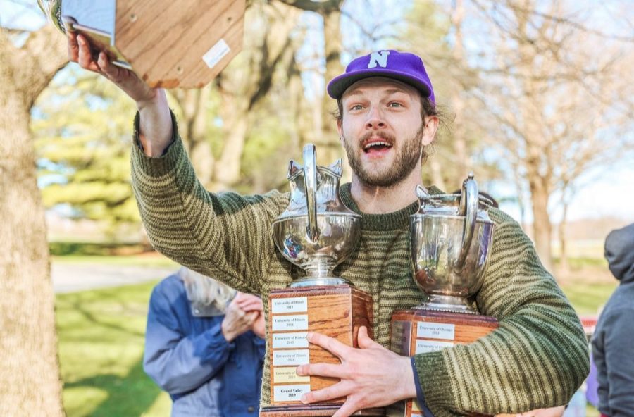 A man in a hat holds a trophy and has two others tucked under his arm.