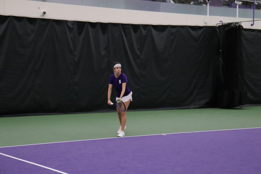 A tennis player in a purple shirt and white skirt prepares to hit a ball.