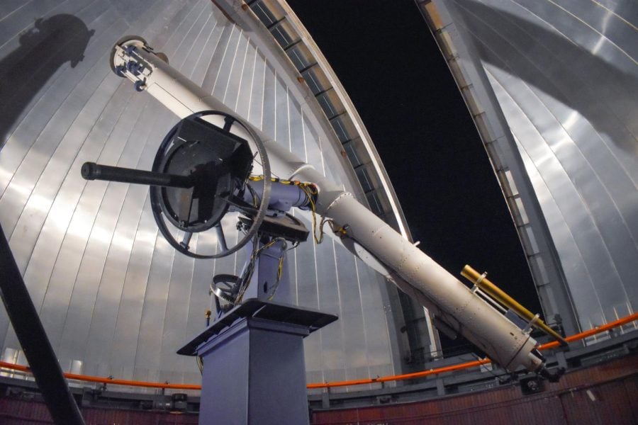 A refracting telescope is shown in the dome of Dearborn Observatory against a dark sky.