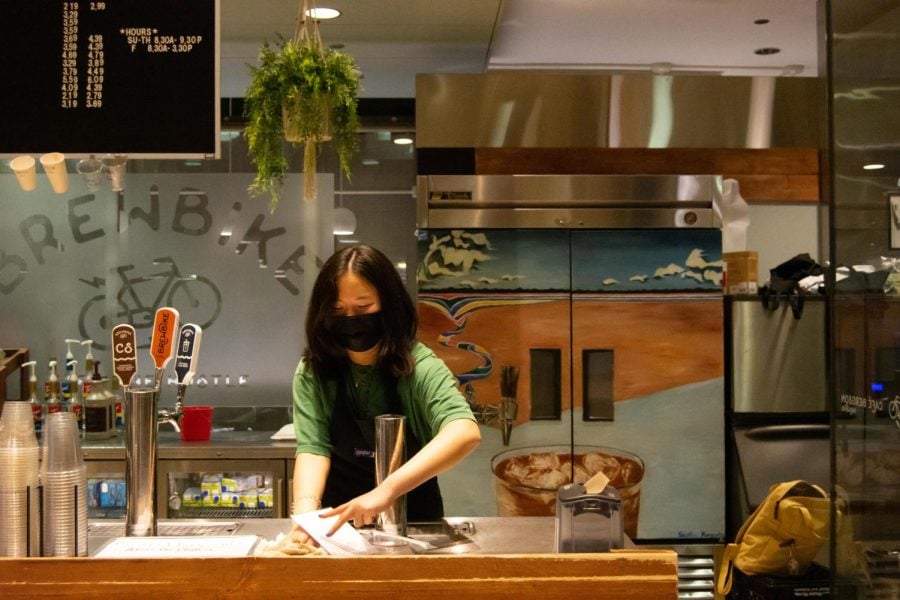 A barista in an apron cleans the counter of a small coffee shop.