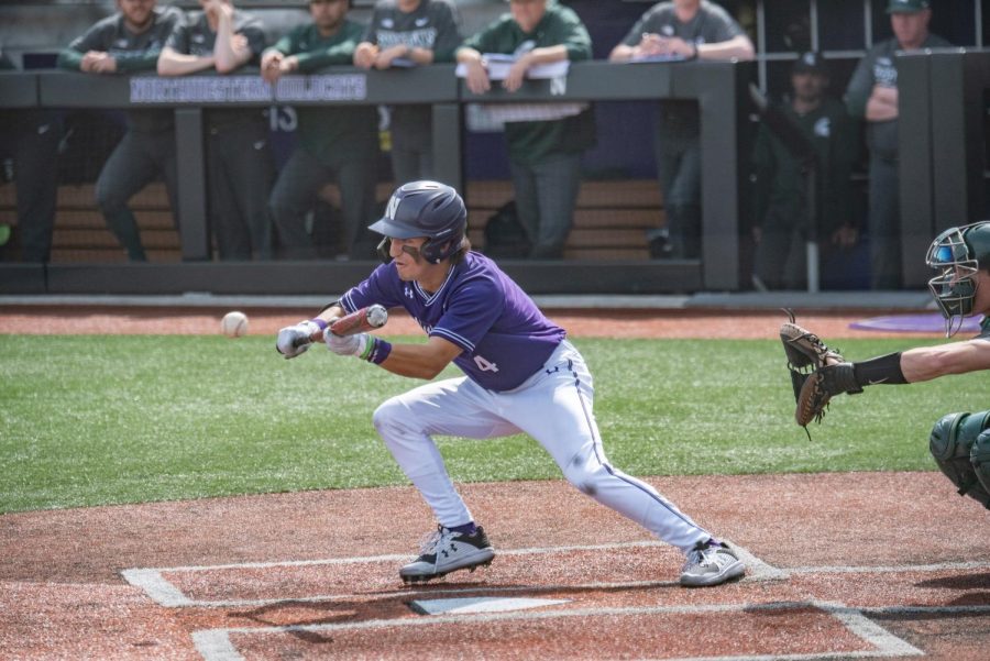 A player wearing a purple jersey holding a baseball bat tries to bunt a baseball.