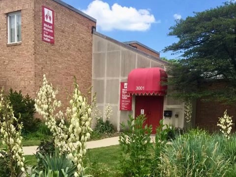 Green grass and plants in front of a red door of the Mitchell Museum