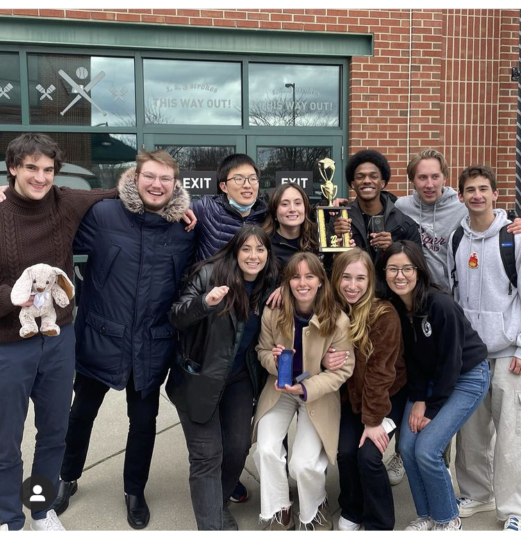 Ten students and a coach from Northwestern’s Mock Trial team huddled together, smiling. Two students each hold an award and the coach holds a stuffed bunny.