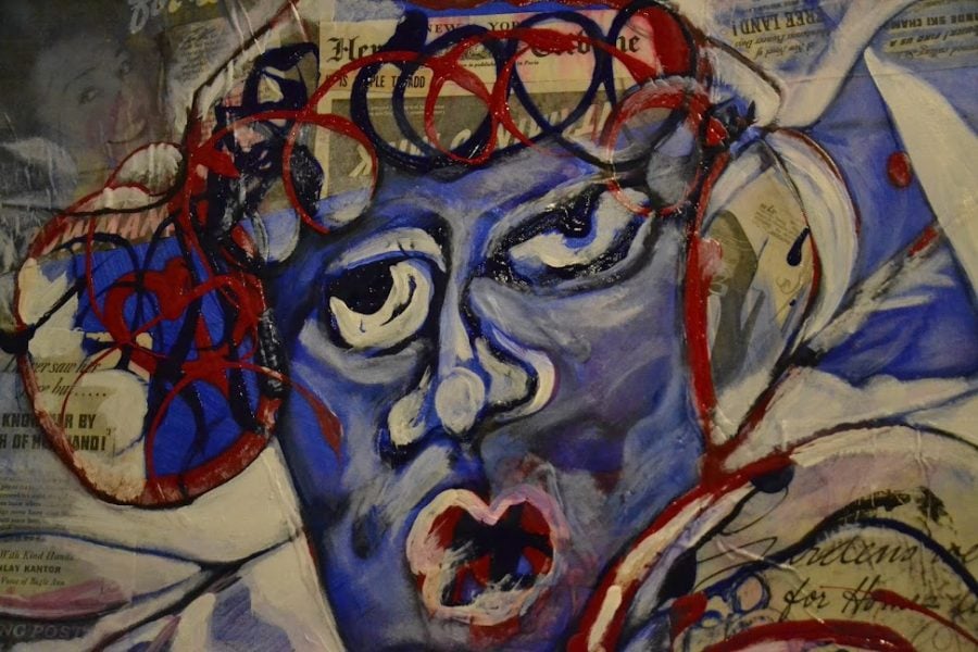 A largely blue painted face is in the center. Red and black curls sit atop their head. There are old newspaper prints laying around the outskirts of the head.
