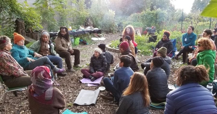 A group sits next to a garden and listens to a panel discussion.
