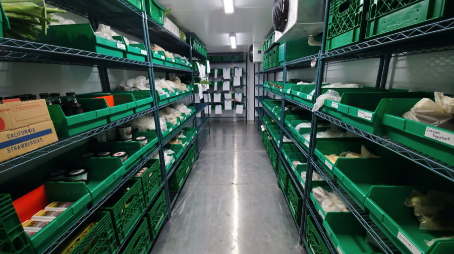 Bags of produce and ingredients are stacked in green containers along walls in a storage room.