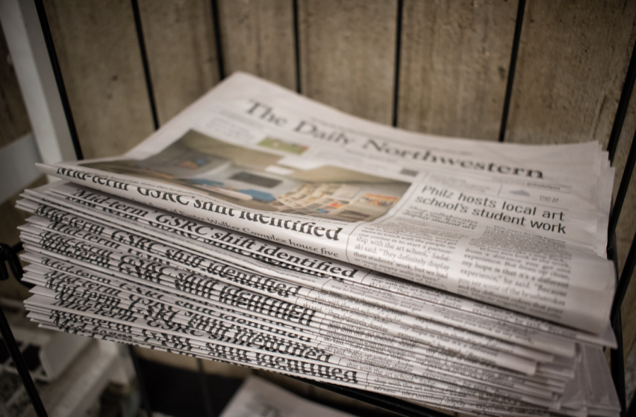 A stack of newspapers in front of a wood-paneled background.