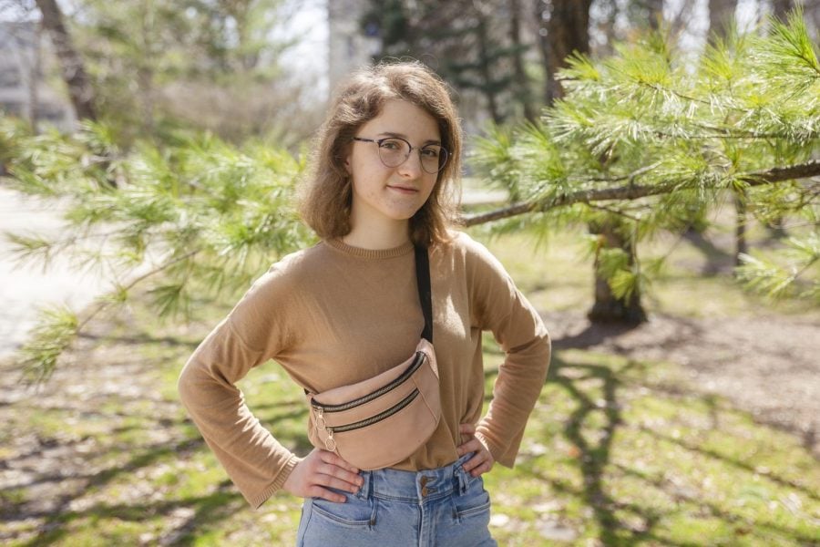 A student stands smiling in front of a tree with hands on hips.
