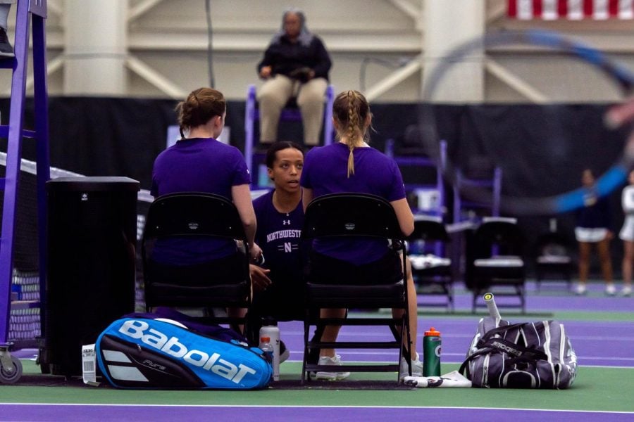 Two tennis players in purple shirts sit during a match.