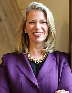 A woman with blonde hair wears a purple blazer and black shirt.