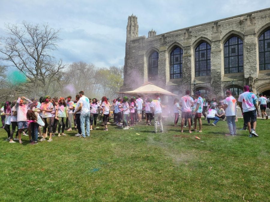 On Deering Meadow, a crowd of students in white shirts throw colorful powder on each other.