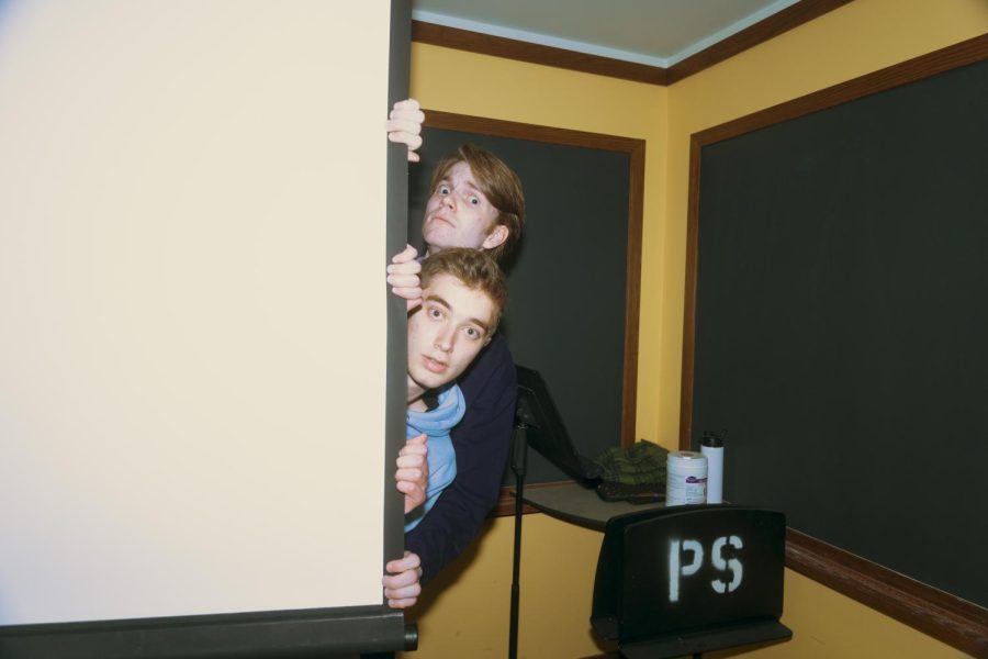 Two people peek out from behind a projector screen. Their faces look surprised, apprehensive.