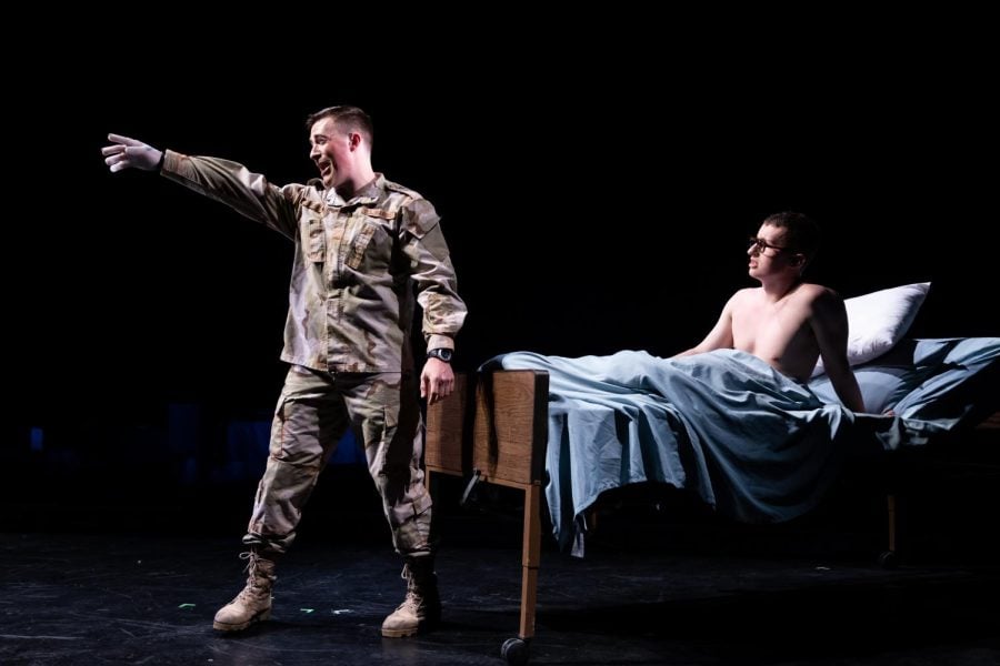 A US soldier points forward as his fellow serviceman watches shirtless from the hospital bed.