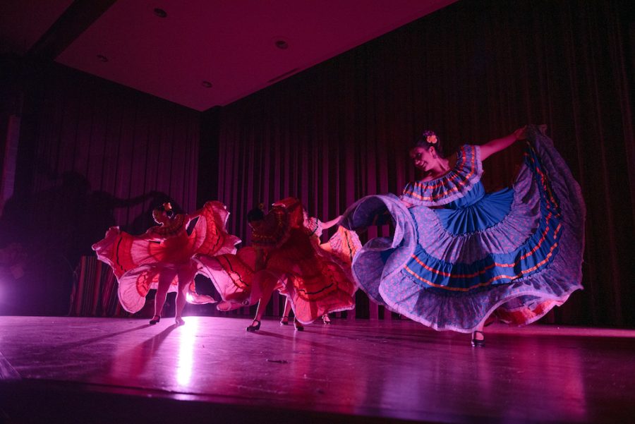 Three female dancers flare the skirts of their multicolored traditional folklórico dresses.