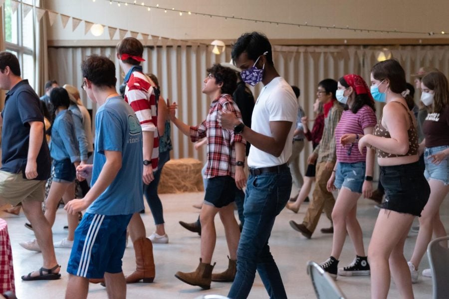 Students participate in a barn dance among hay bales and string lights.