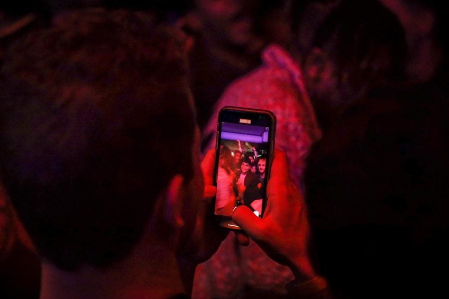 A student records a crowd on their phone. Red lights shine around them.