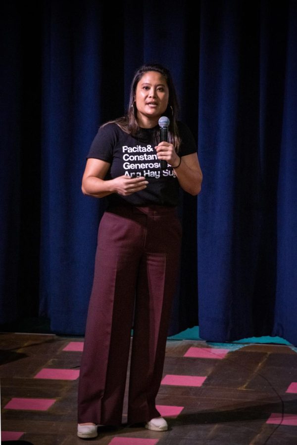 Justine Ang Fonte stands on stage with a microphone. She waves her stands passionately while speaking.