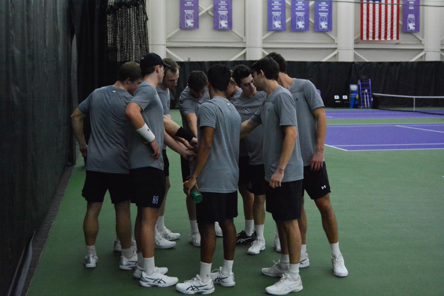 Tennis+players+in+gray+shirts+and+black+shorts+huddle+on+green+and+purple+court.