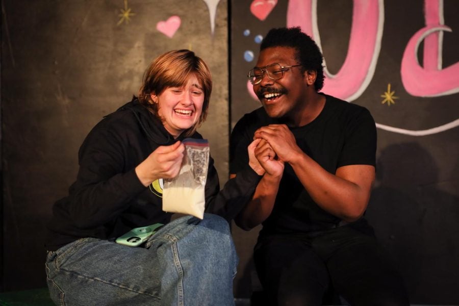 Two people in black shirts smile and look at a plastic storage bag full of milk. The person on the left holds the bag.