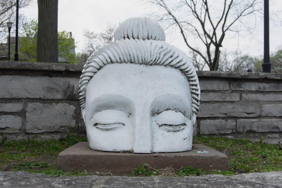 A statue of a white Buddha head emerging from the ground.