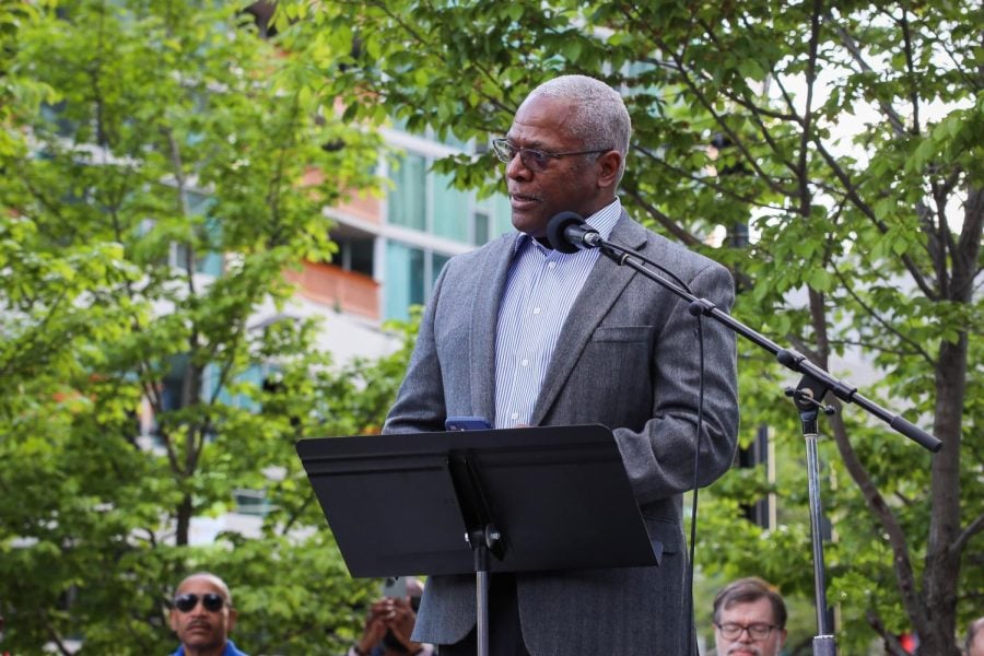 Rev. Michael Nabors, wearing a suit, speaks into a microphone while looking to the left.