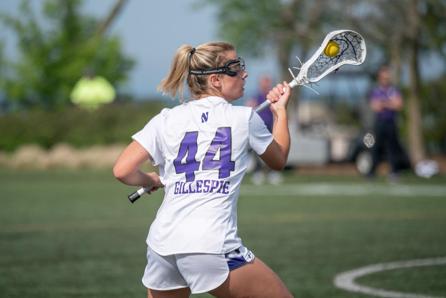 A player in a white jersey holding a lacrosse stick catches and cradles the ball.