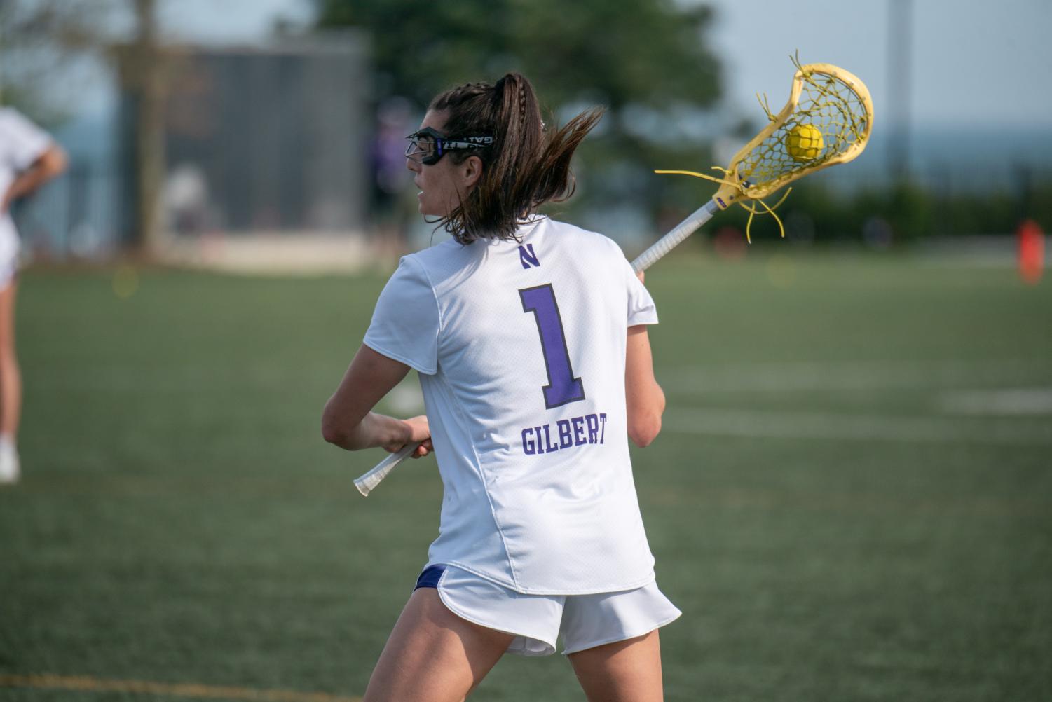 A player in a white jersey holding a lacrosse stick with a ball prepares to make a free position shot.