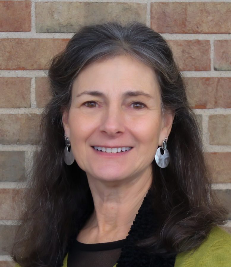 A head shot of Karen Singer in a green sweater standing in front of a brick wall.