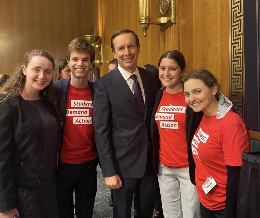 Students wearing matching red shirts that say “Students Demand Action” pose with a man in a suit.