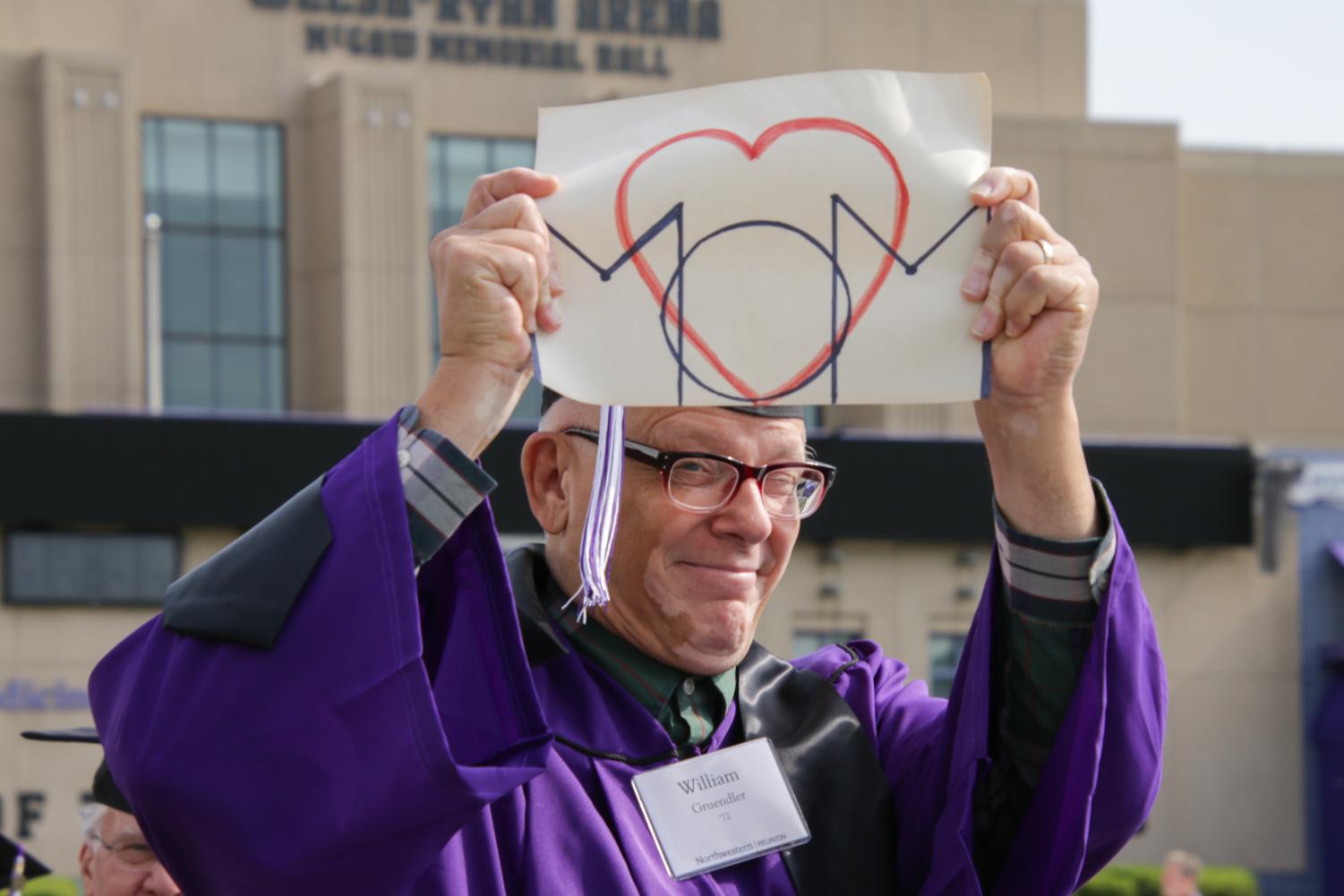 A person in a purple gown holds up a white sign with a red heart and black lines.