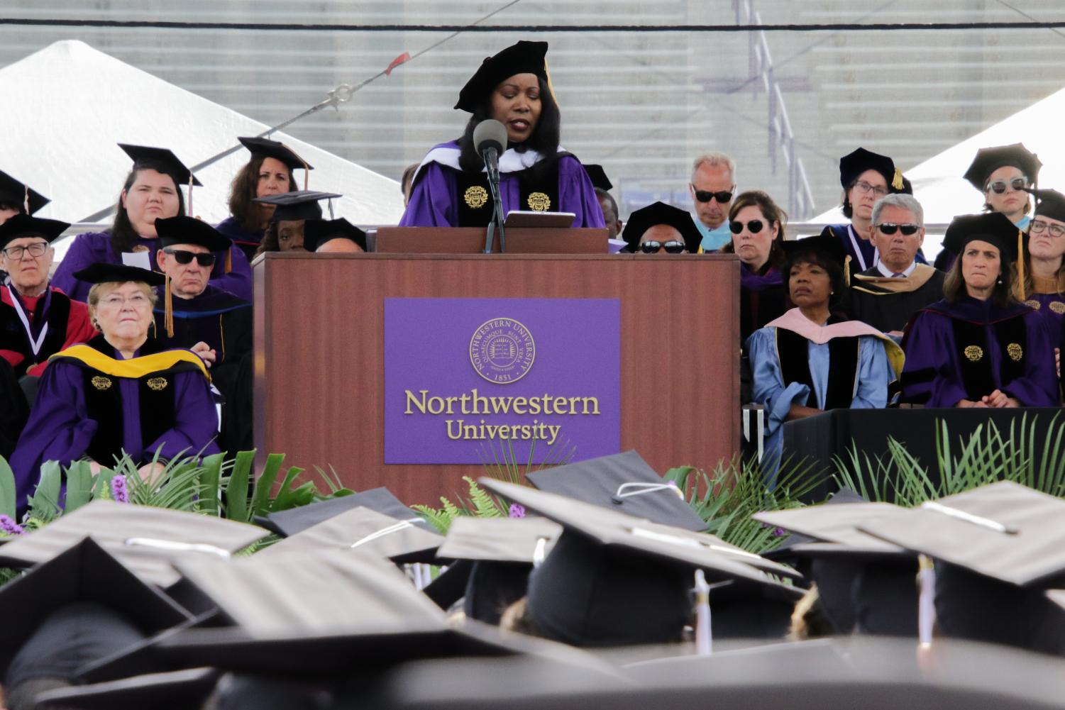  A person in a purple gown and graduation cap speaks in front of a brown podium.