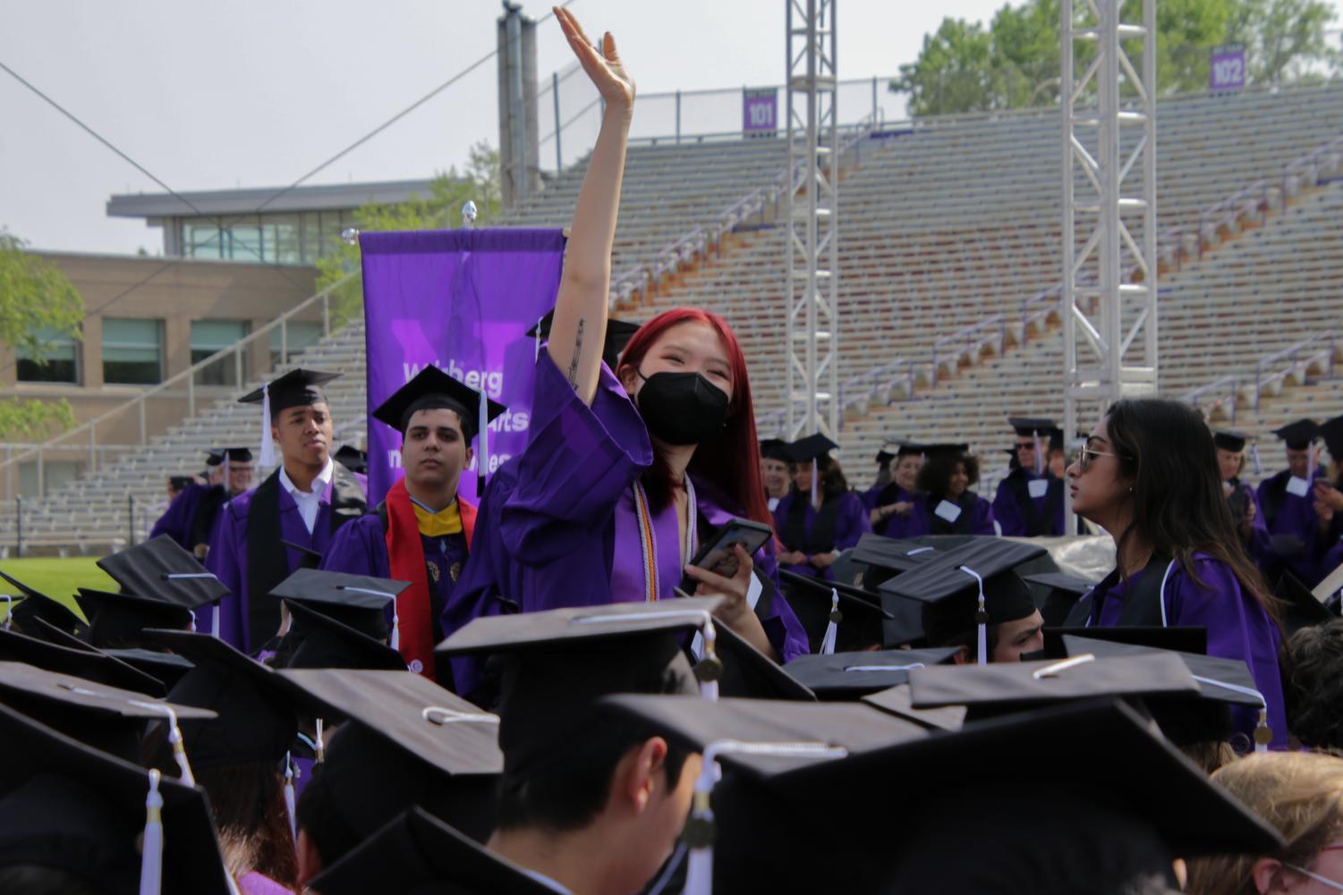 A student in a cap and gown raises their arm up amid a sea of graduation caps.