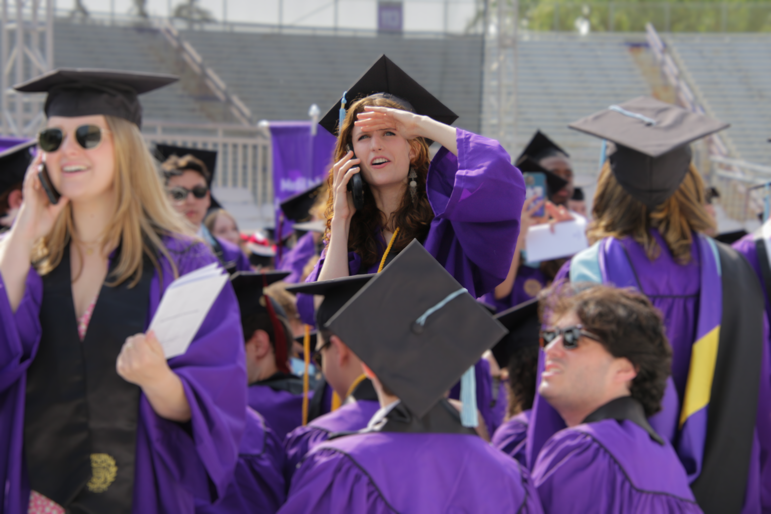 A person in a cap and gown looks to the crowd as they hold their cell phone in the other hand.