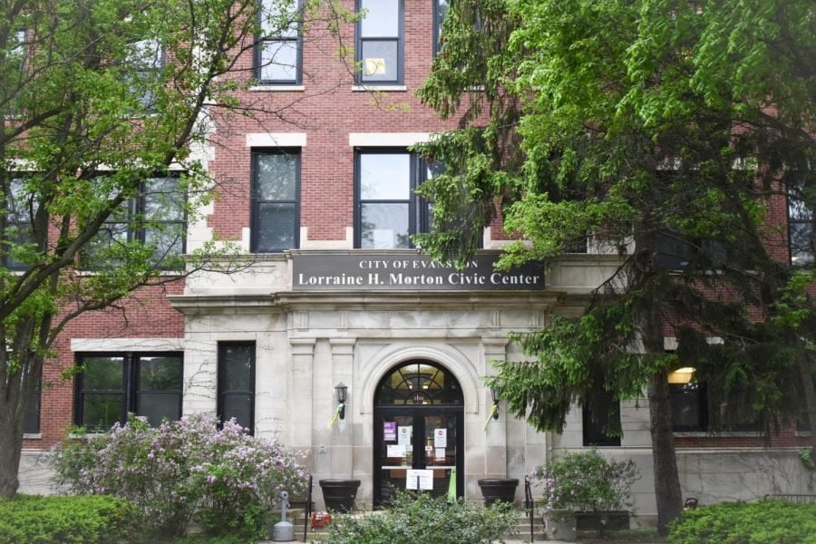 The Lorraine H. Morton Civic Center. Green trees grow around the red brick building, a dark-brown sign saying “The City of Evanston” is front and center.