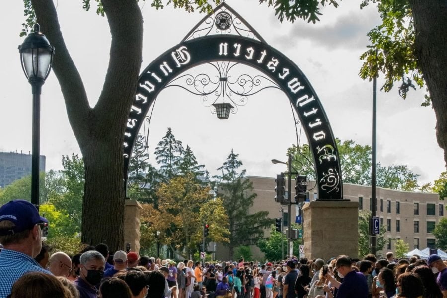 Dark-colored arch that reads “Northwestern University” with a crowd of people standing under it.