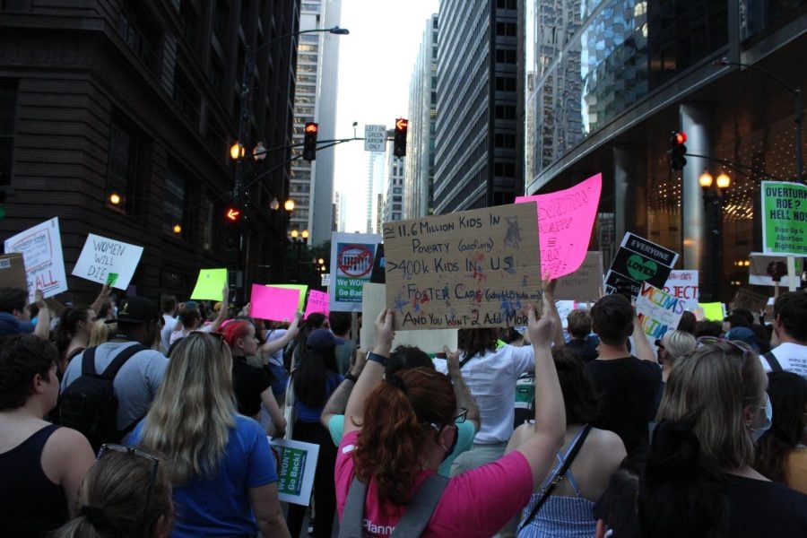 A crowd of protesters holds signs on a street lined with skyscrapers.