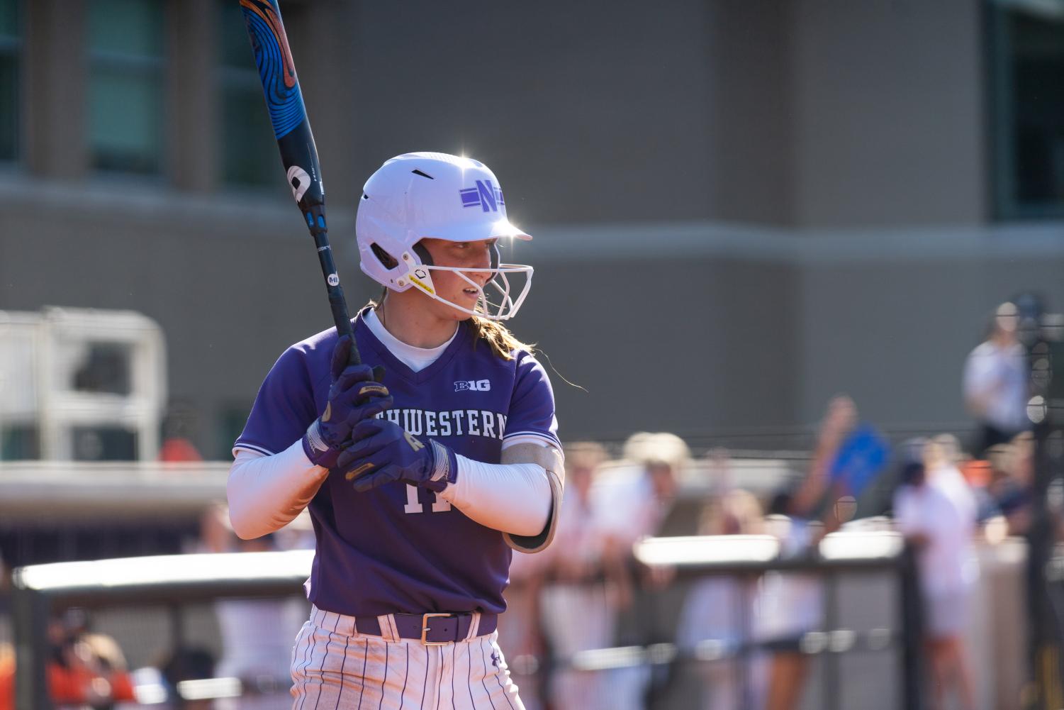 Softball+player+in+purple+uniform+and+cap+holds+a+blue-and-black+bat+on+right+shoulder.